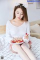 A woman sitting on a bed holding a plate of cherries.