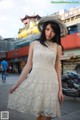 A woman in a white dress and hat standing on a sidewalk.