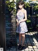 A woman in a white dress standing in front of a brick wall.