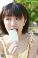 A woman in a yellow and white dress eating a popsicle.