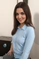 A woman in a blue shirt sitting on a desk.