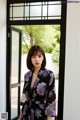 A woman standing in front of a door wearing a black and purple floral robe.